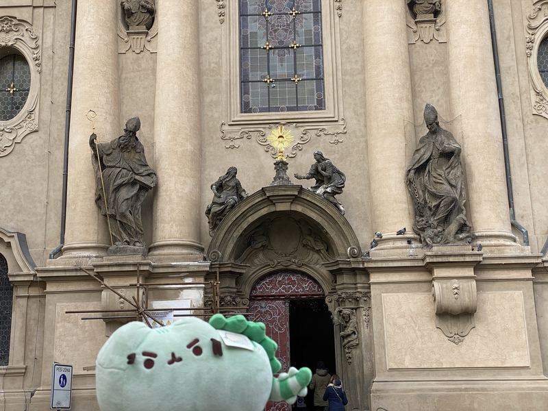 Pusheeno held up in front of an ornate baroque church facade with statues
