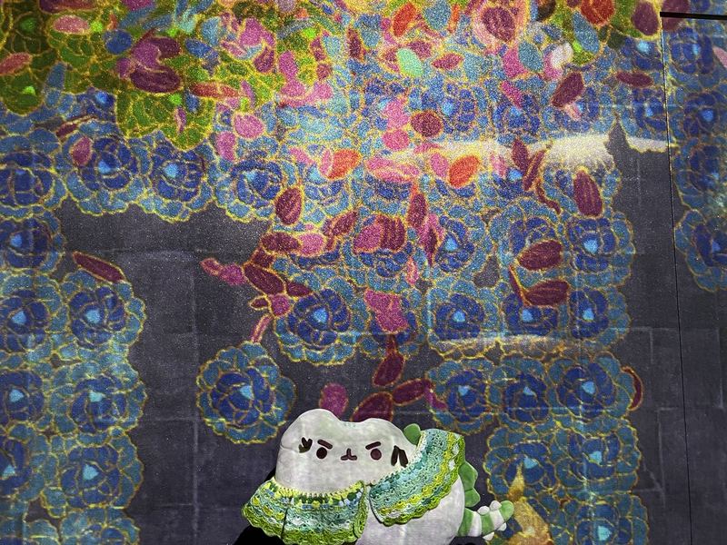 Pusheeno in his crocheted collar in front of a wall of glittering projected flowers