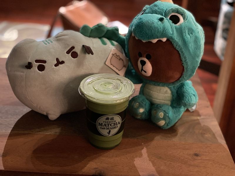 Pusheeno and Dino Brown on a wooden table with an iced matcha latte between them