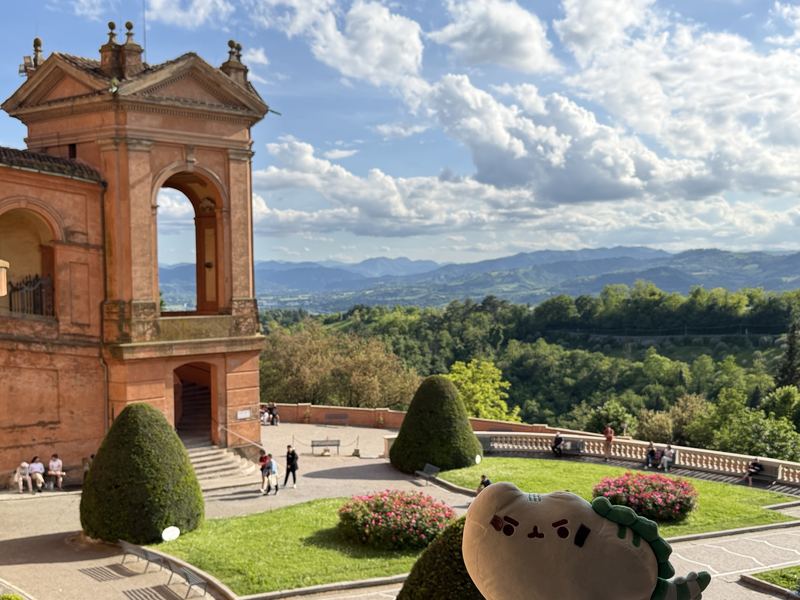 Pusheeno in front of the orange arcades of the Sanctuary of San Luca, with green hills beyond