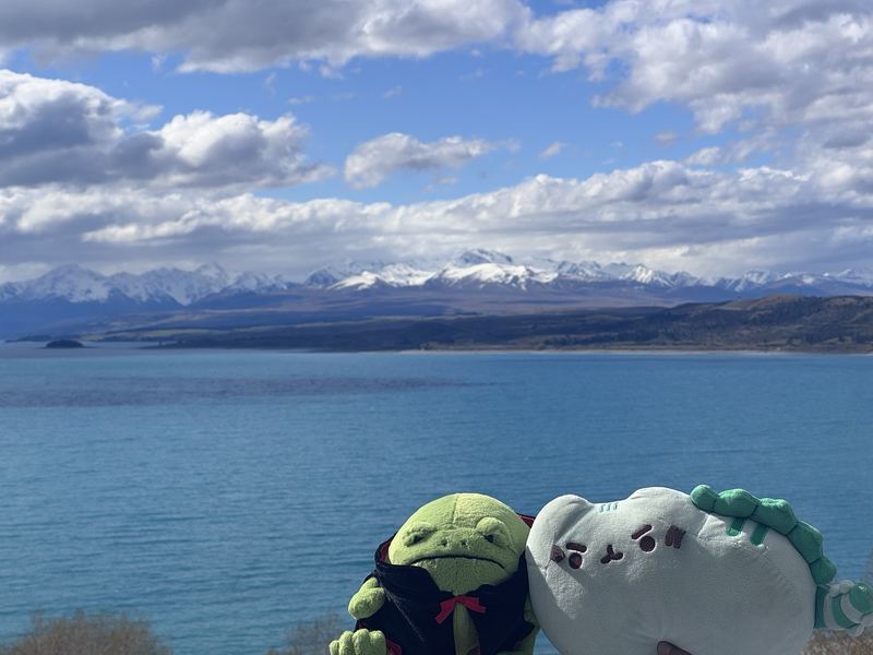 Pusheeno and Ricky in front of a glacier-blue lake with snow-capped mountains behind