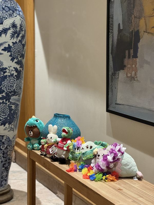 Dino Brown, little Gunnersaurus, Miffy, Gunnersaurus, Pusheeno and Mersheen in a row on a wooden bench, the last two wearing flower leis